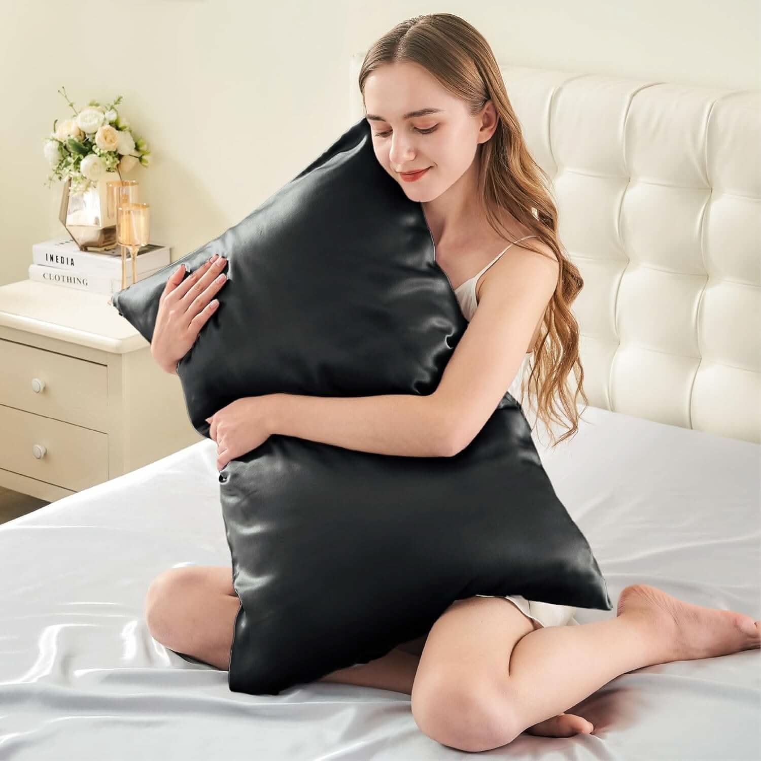 Woman sitting on a bed hugging a black silk pillowcase, showcasing its smooth, luxurious texture and softness for ultimate comfort