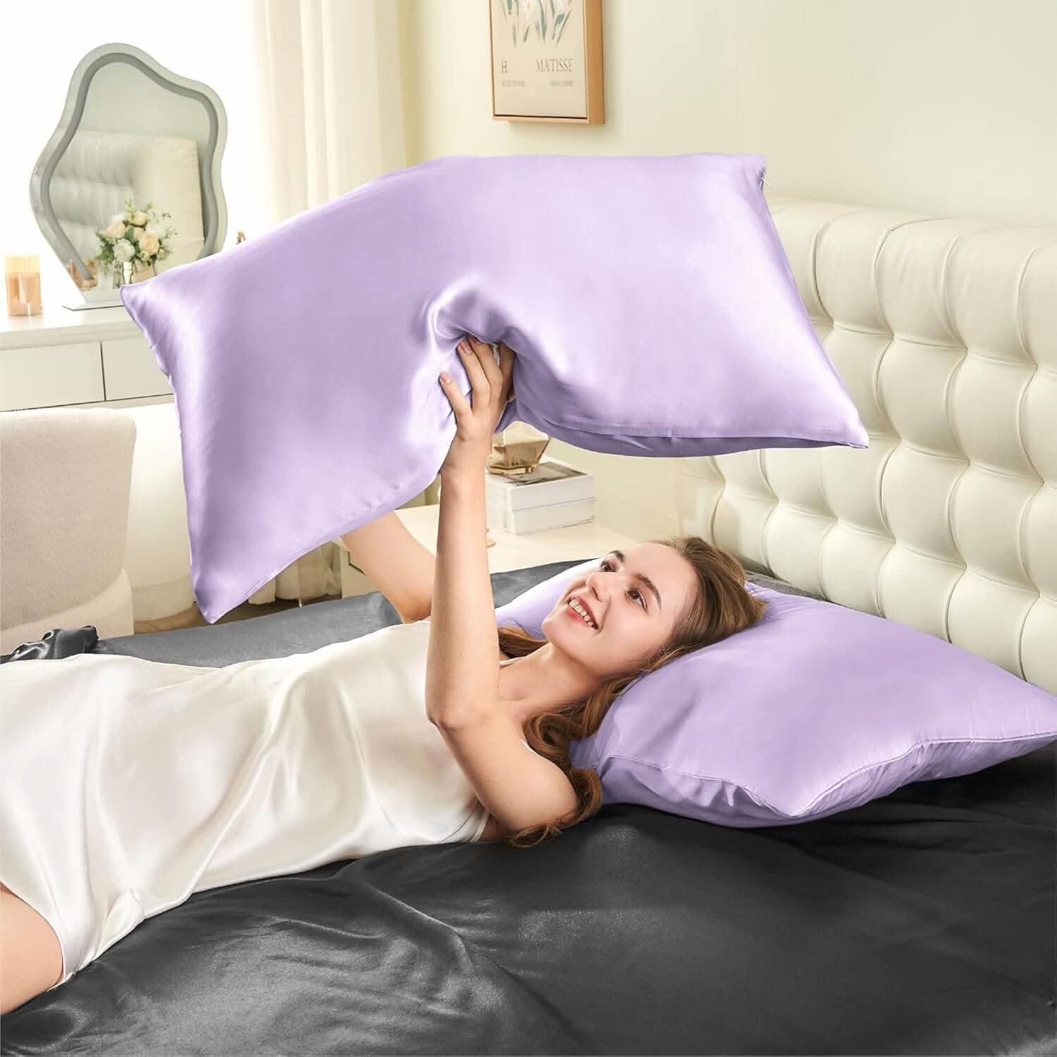 Woman lying on a bed joyfully tossing a lavender silk pillowcase in the air, showcasing its soft and smooth texture.