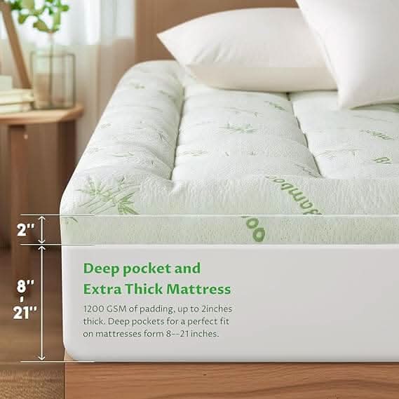 Close-up of a white quilted mattress topper on a neatly made bed, highlighting its thick padding and elasticized edges for a secure fit and added comfort.