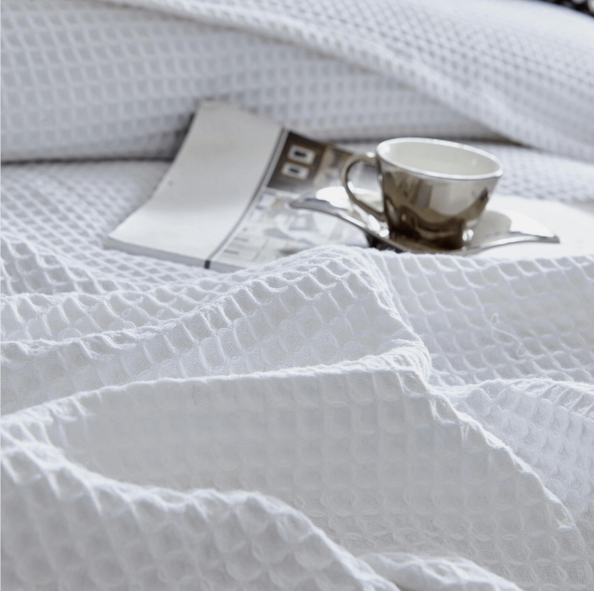Cozy white bedding with a cup of coffee and an open magazine on a bed.