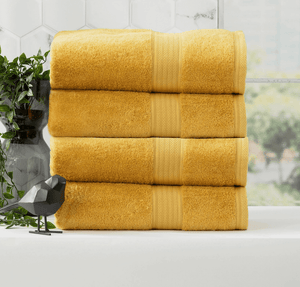 Stack of four yellow bath towels next to a geometric bird sculpture and a green plant in a bathroom.