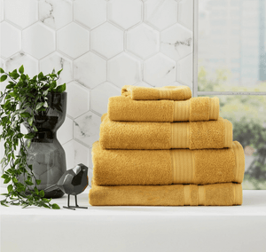A stack of folded yellow towels next to a black vase with green plant and decorative bird on a white countertop