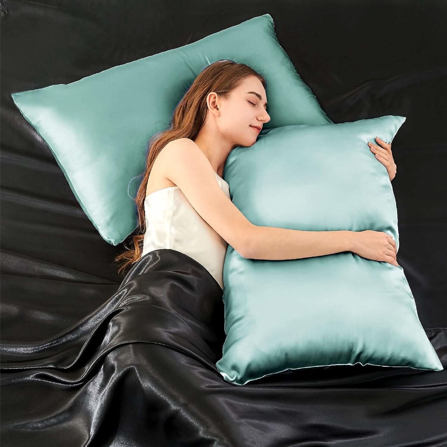 Woman lying on a bed hugging a light blue silk pillowcase, showcasing its smooth and luxurious texture