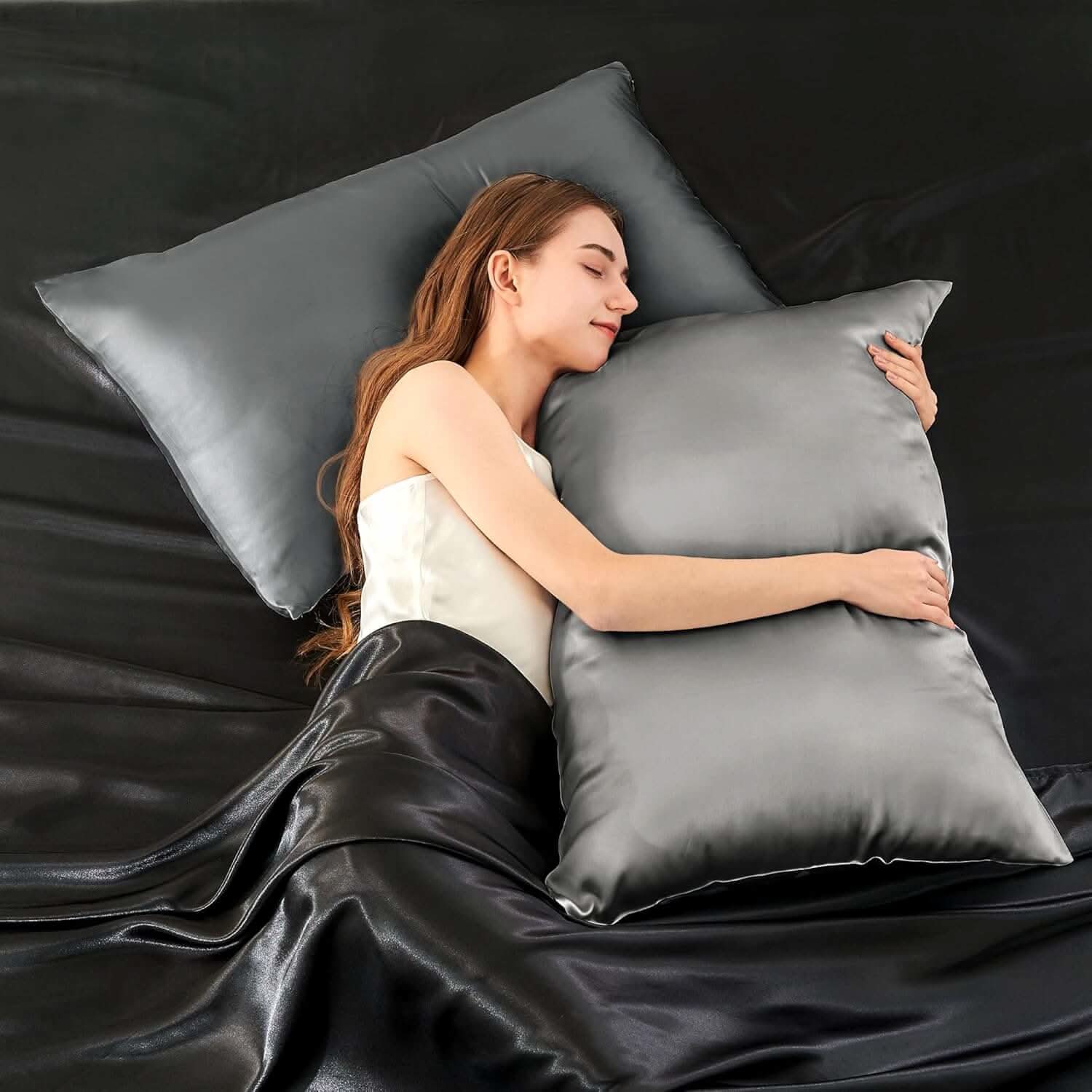 Woman lying on a bed hugging a silver silk pillowcase, highlighting its smooth and luxurious texture.