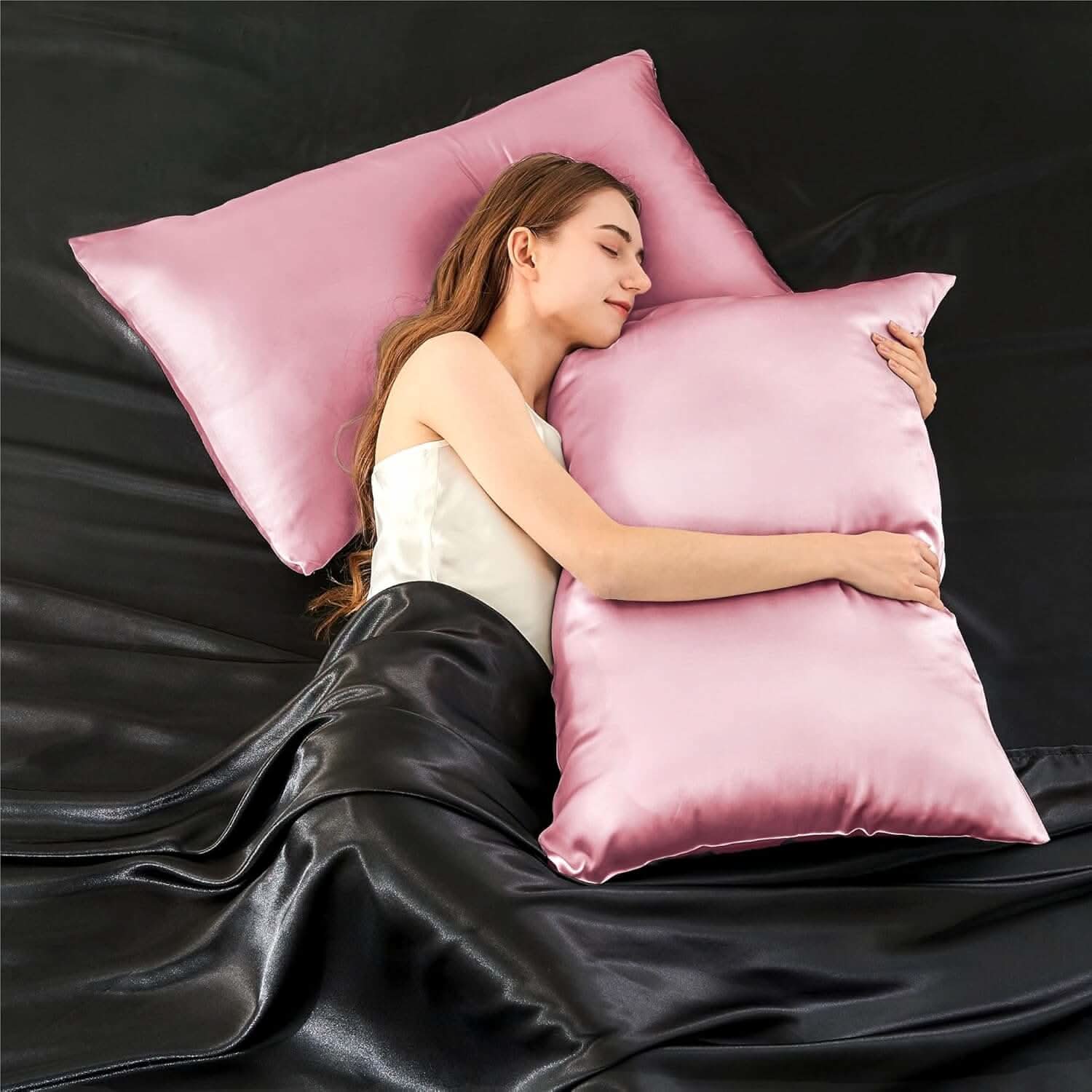Woman lying on a bed hugging a pink silk pillowcase, highlighting its smooth and luxurious texture.