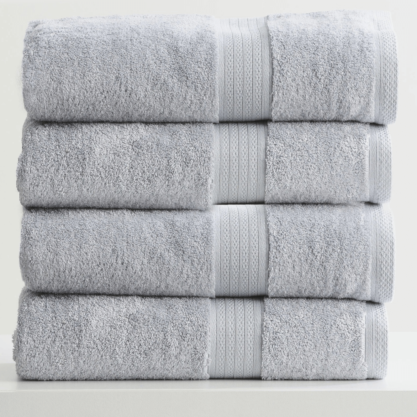 Stack of four soft, grey towels neatly folded on a white surface