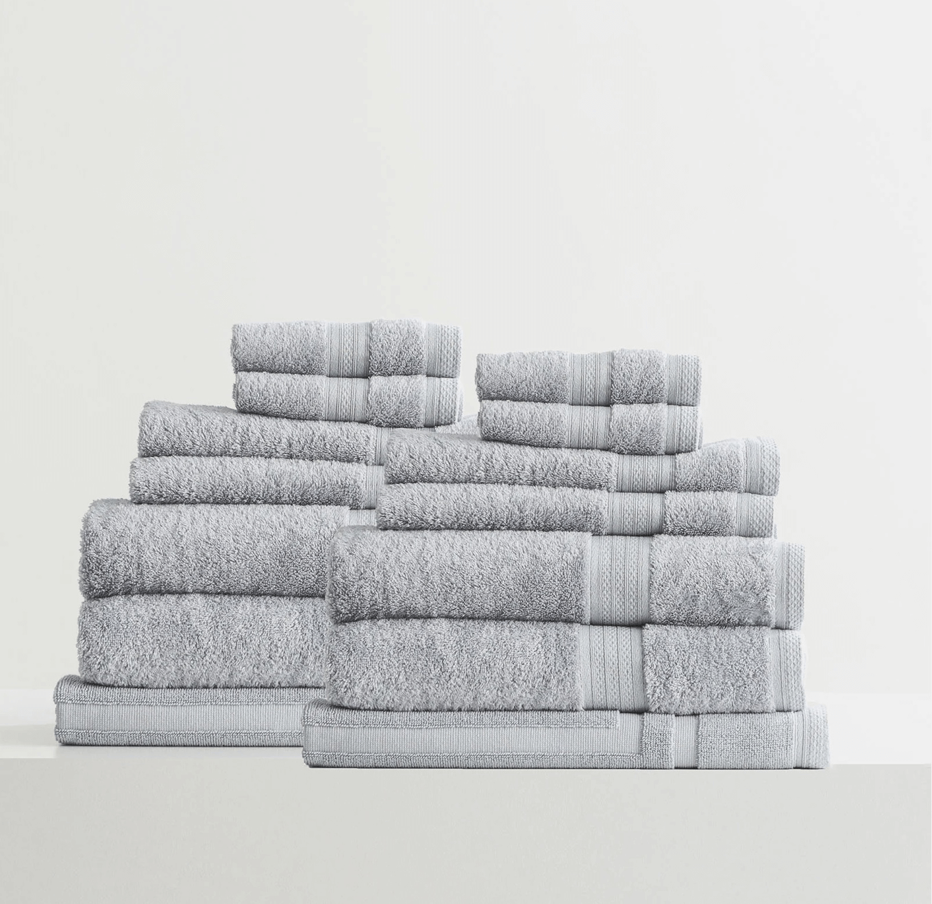 Set of neatly stacked gray bath towels in various sizes on a white surface.